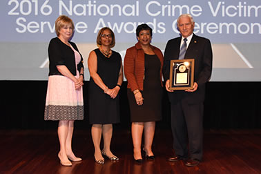 National Crime Victim Service Award recipient Dr. John P.J. Dussich with (from left) Joye E. Frost, Director, Office for Victims of Crime; Karol V. Mason, Assistant Attorney General; and Attorney General Loretta E. Lynch.