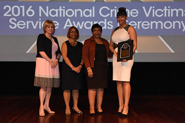 National Crime Victim Service Award recipient Brenda Tracy with (from left) Joye E. Frost, Director, Office for Victims of Crime; Karol V. Mason, Assistant Attorney General; and Attorney General Loretta E. Lynch.
