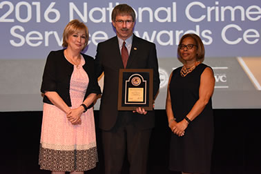 National Crime Victims’ Service Award recipient Russell P. Butler accepts the award with (from left) Joye E. Frost, Director, Office for Victims of Crime and Karol V. Mason, Assistant Attorney General.