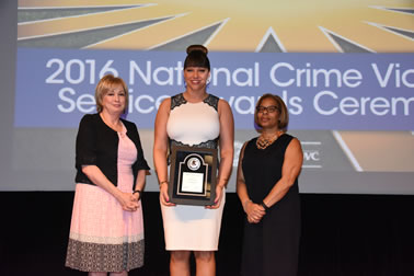 National Crime Victims’ Service Award recipient Brenda Tracy accepts the award with (from left) Joye E. Frost, Director, Office for Victims of Crime and Karol V. Mason, Assistant Attorney General.